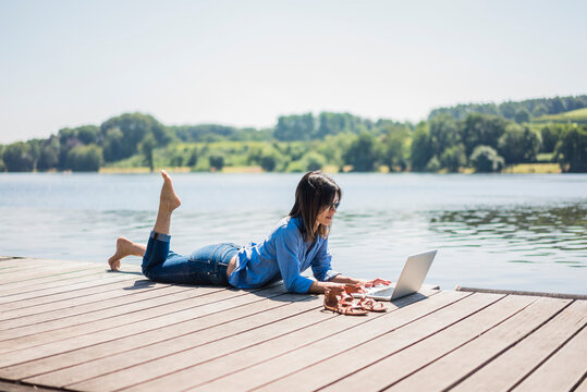 Mature woman working at a lake, using laptop on a jetty