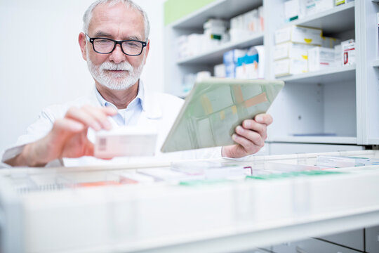Pharmacist with tablet and medicine at cabinet in pharmacy