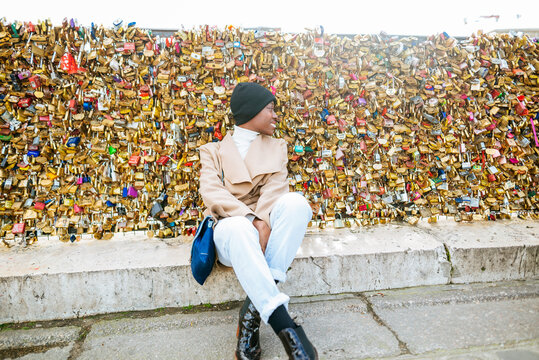 Young woman sitting against love locks on bridge, Paris, France
