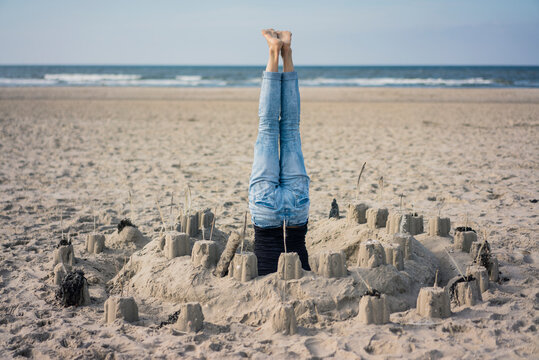 Mature woman doing a headstand on the beach in a sandcastle