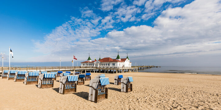 Germany,ÔøΩMecklenburg-WesternÔøΩPomerania, Heringsdorf, Hooded beach chairs on sandy coastal beach with pier in background