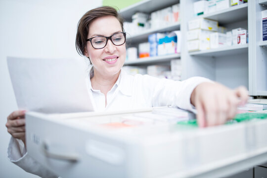 Smiling pharmacist seeking out medicine at cabinet in pharmacy