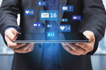 Close up of businessman hands holding tablet with social media icons on blurry background. Communication, network, connections, device and app concept.