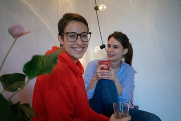 Two girlfriends at home sitting in kitche, talking and drinking tea