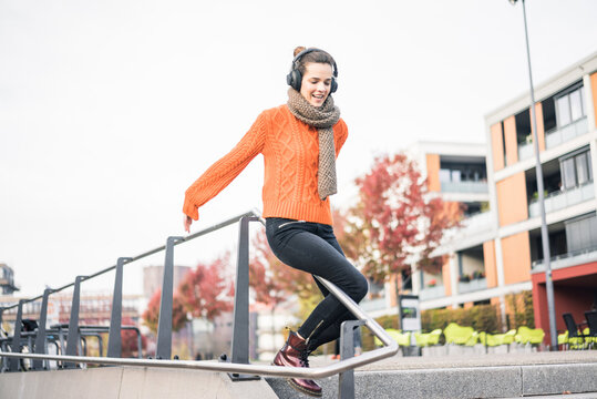 Portrait Of Laughing Woman With Cordless Headphones Sliding Down A Banister