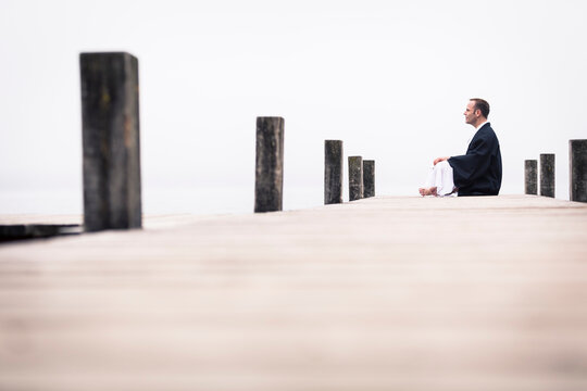 Man sitting on jetty doing yoga exercise, Lake Starnberg, Germany