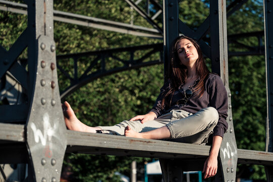 Young woman enjoying the evening sun, sitting on a bridge
