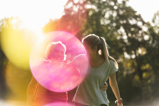 Fit grandmother and granddaughter walking in park with arms around