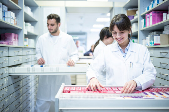 Smiling pharmacist seeking out medicine at cabinet in pharmacy