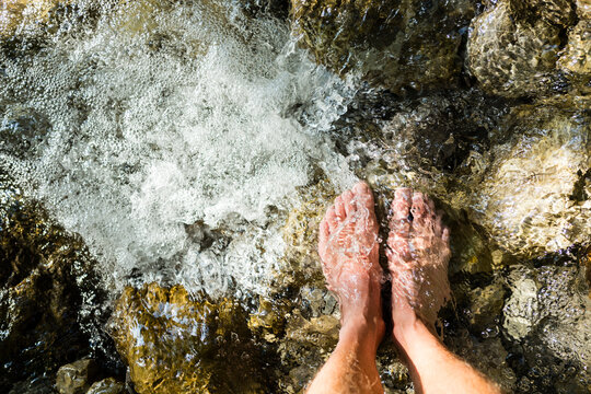 Man's feet standing on stone in a brook
