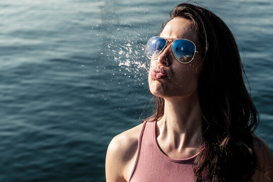 Portrait of young woman wearing sunglasses snorting water