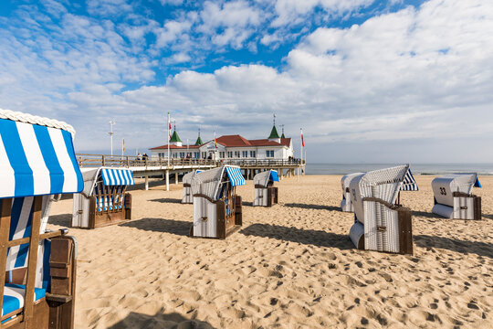 Germany, Mecklenburg-Western Pomerania, Heringsdorf, Hooded beach chairs on sandy coastal beach with pier in background