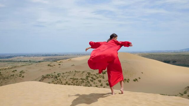 sexy brunette woman in a red satin long dress walks on sand dunes in the desert