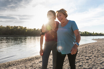 Fit grandmother and granddaughter walking at the river with arms around, having fun