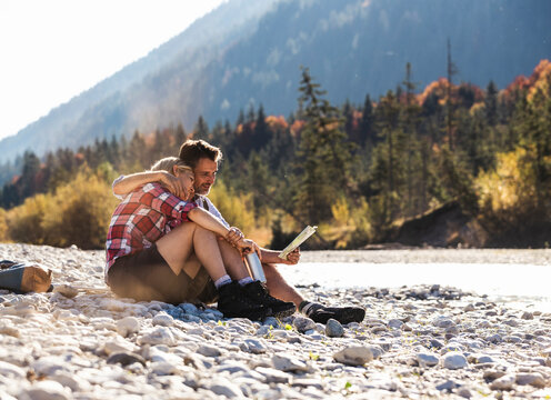 Austria, Alps, couple on a hiking trip having a break at a brook reading map