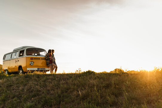Young couple leaning on their camper, watching ghe sunset