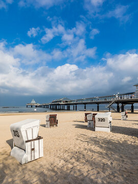 Germany, Mecklenburg-Western Pomerania, Heringsdorf, Clouds over hooded beach chairs on sandy coastal beach with pier in background