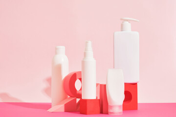 several different white plastic bottles and tube on pink geometric podiums on pink background