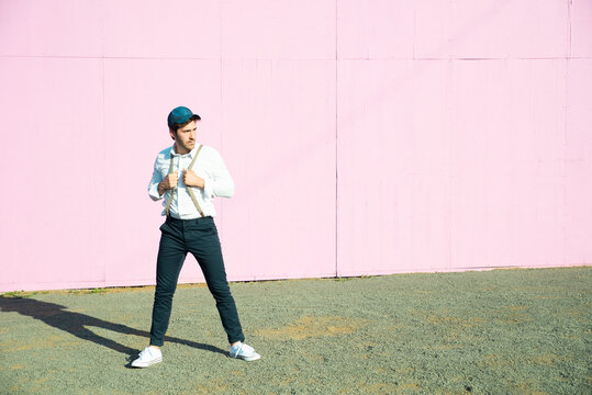 Young man in front of pink construction barrier, holding onto his suspenders
