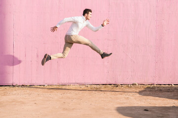 Exuberant young man jumping in front of pink wall