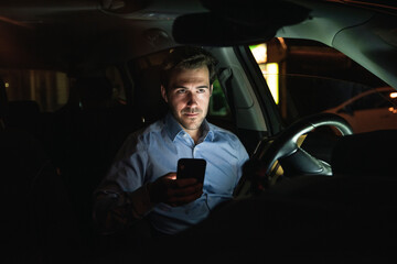 Young man using cell phone in car at night