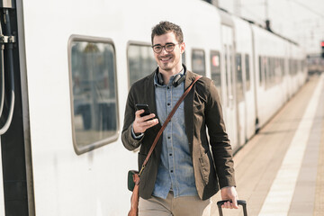 Smiling young man with cell phone at station platform