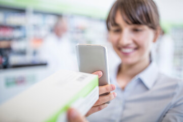 Smiling woman in pharmacy holding smartphone and medicine