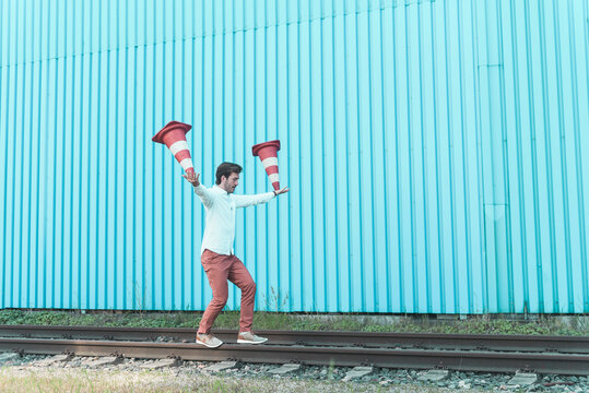 Young man balancing on rails, juggling traffic cones