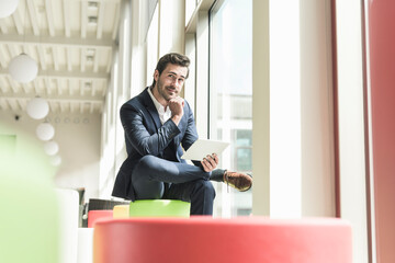 Young businessman sitting in lounge, using digital tablet