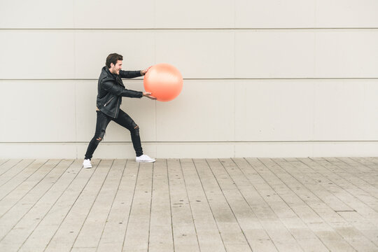 Young man in leather jacket, playing with a gym ball