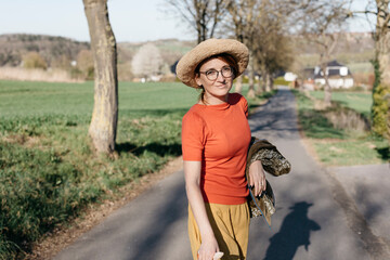 Portrait of smiling mature woman wearing glasses and straw hat standing on country road