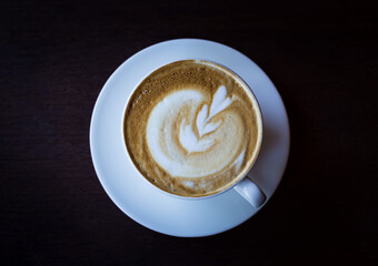 A cup of coffee with heart pattern in a white cup on the dark wooden background