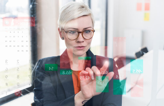 Businesswoman touching glass wall with data in office