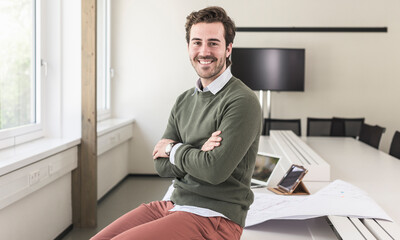 Successful, young businessman sitting in boardroom with arms crossed