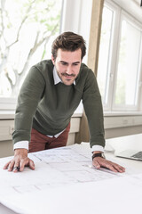 Young architect working on blueprint in bright office