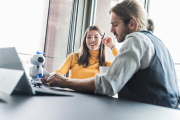 Young businesswoman and businessman sitting at desk in office talking