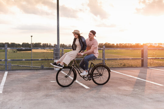 Happy young couple together on a bicycle on parking deck at sunset