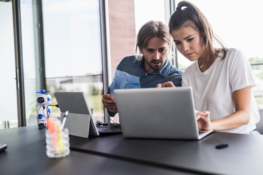 Young man and woman working together on laptop at desk in office
