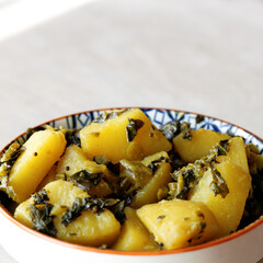 Fried dish with potatoes and kale leaves in bowl. Indian vegetarian cuisine Subji meal.