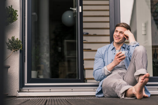 Smiling man taking a break, drinking coffee in front of his home