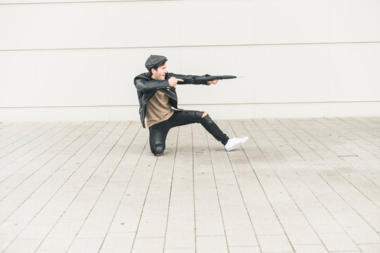 Young man pretending to shoot with closed umbrella