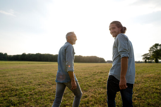 Happy father and adult son walking on a meadow in the countryside