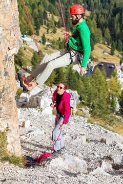 Italy, Cortina d'Ampezzo, man abseiling in the Dolomites mountains with the assistance of a woman