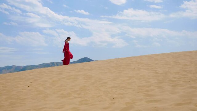 sexy brunette woman in a red satin long dress walks on sand dunes in the desert