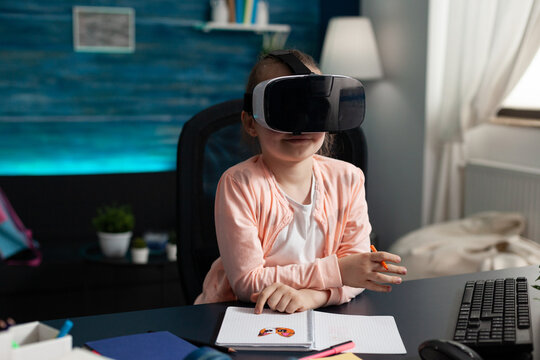 Children experiencing virtual reality using headset while sitting at desk table in living room during online lesson. Concept of distance education for kids at home during coronavirus quarantine - Powered by Adobe