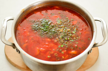 Ukrainian borscht in a saucepan on a light background.
