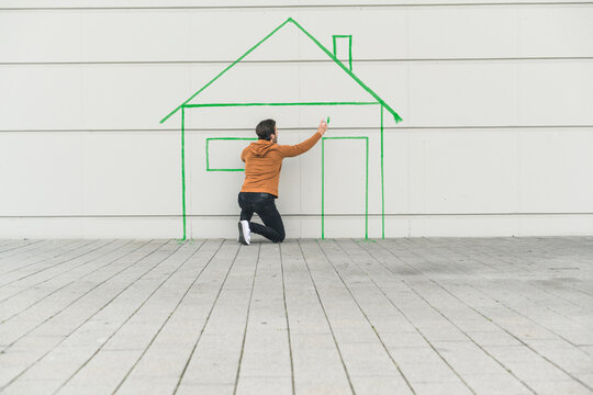 Digital composite of young man drawing a house at a wall