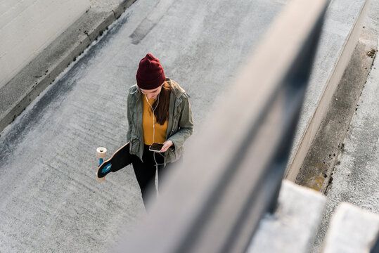 Stylish young woman with skateboard and cell phone on parking deck
