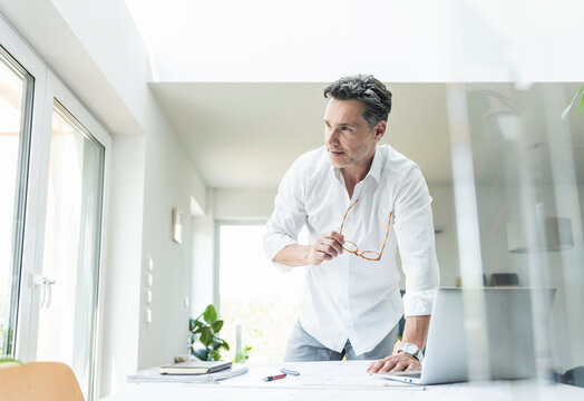 Architect working on blueprint in a bright office, using laptop