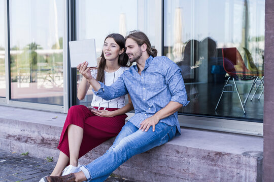 Young couple sitting on windowsill at a building using a tablet